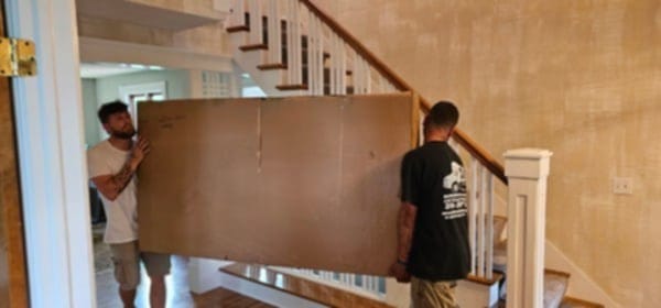 Professional movers carrying a large heavy box safely through a home without using a hand cart