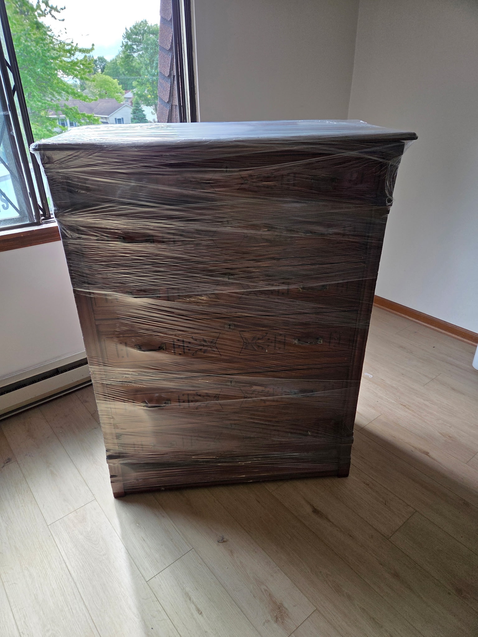Shrink-wrapped wooden dresser prepared by Reliable Movers to secure drawers and protect furniture during a residential move