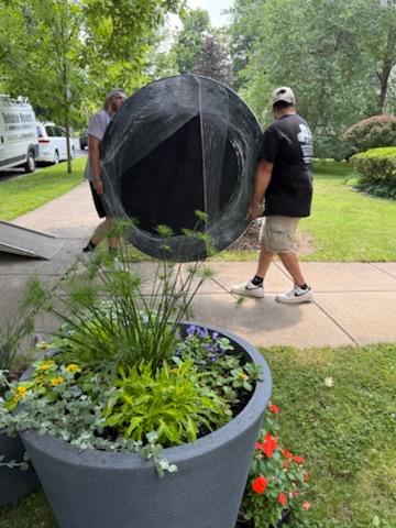 Reliable Movers carrying a large round dining table wrapped for protection during a residential move in Clinton, New York.