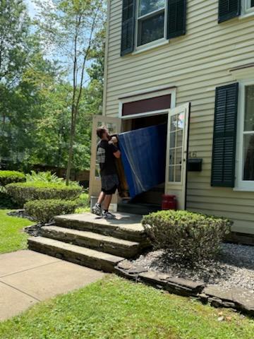 Reliable Movers carrying a large wrapped furniture piece through the front entrance of a historic home in Clinton, NY.