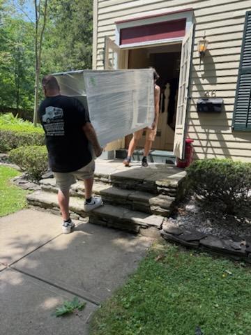Reliable Movers carrying a fully wrapped furniture piece from a Victorian home during a residential move in Clinton, New York.