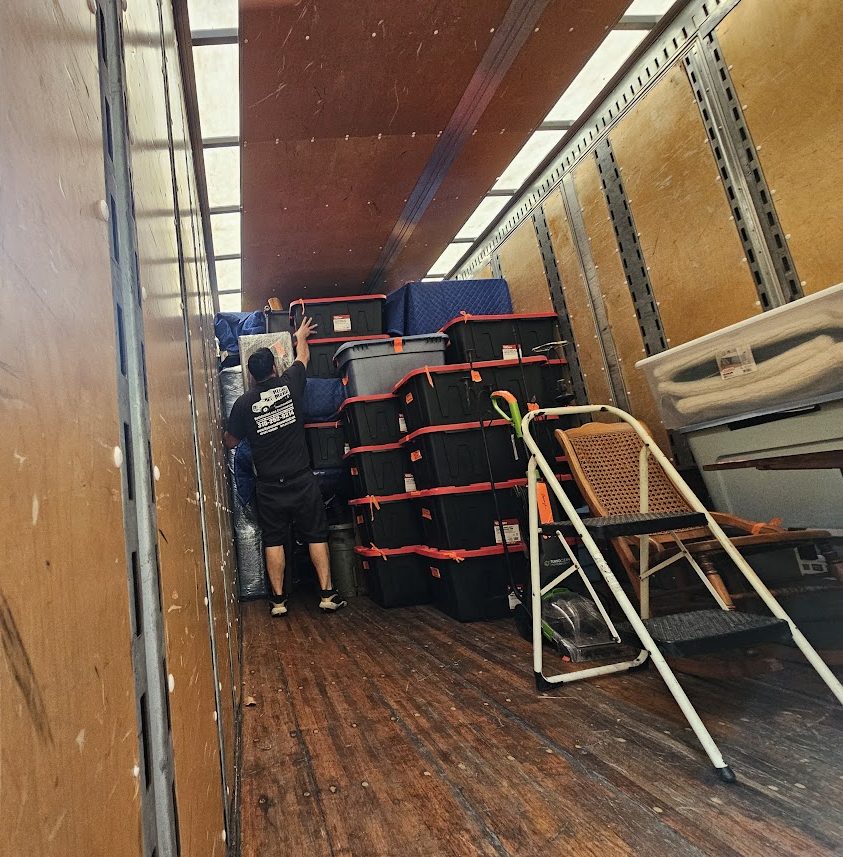 Reliable Movers employee loading and securing storage totes and household furniture inside a moving truck
